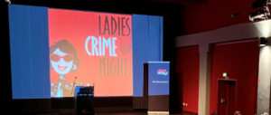 Das Word-Bildlogo der Mörderischen Schwestern ist auf eine Kinoleinwand projiziert. Eine gezeichnete Frau in rot, weiß und schwarz neben den Wortern: Ladies Crime Night.